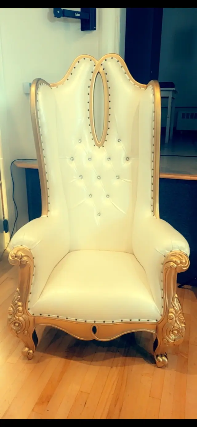 White tufted throne chair with a carved gold frame on a wood floor