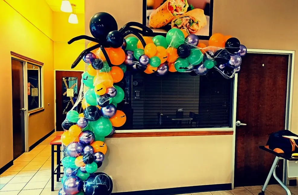 Halloween balloon arch in orange, black, teal and purple framing a reception desk