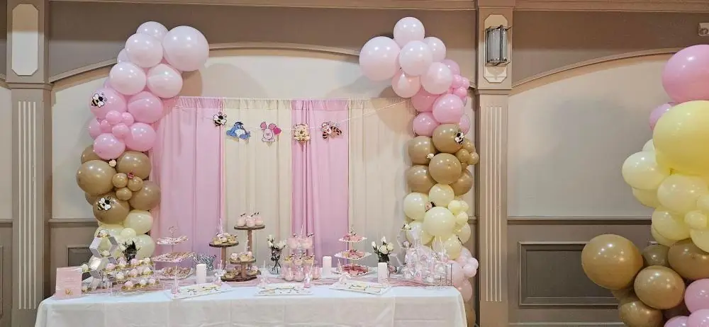 Pink, white and beige balloon arches around a dessert table against a pink curtain backdrop