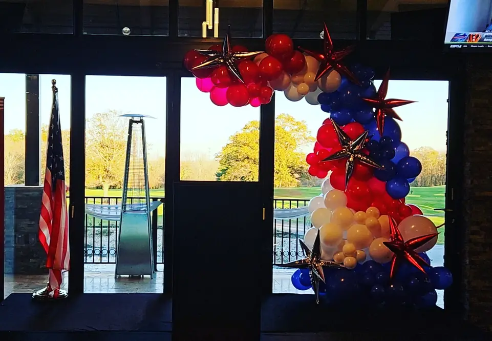 Red, white and blue balloon arch with star foils framing a venue's glass doors